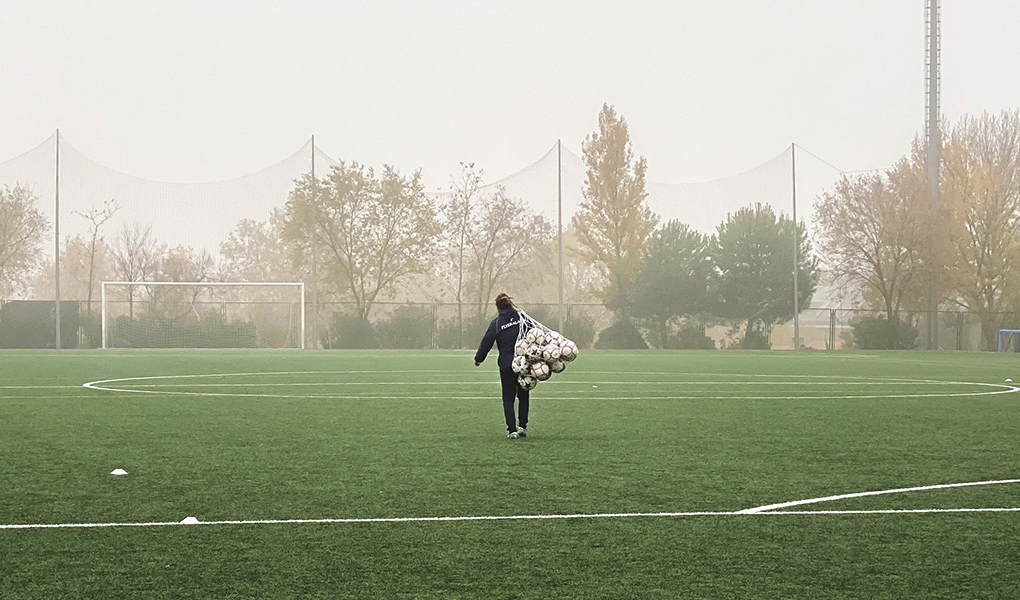 Kuvassa valmentaja kantaa jalkapallosäkkiä kentällä