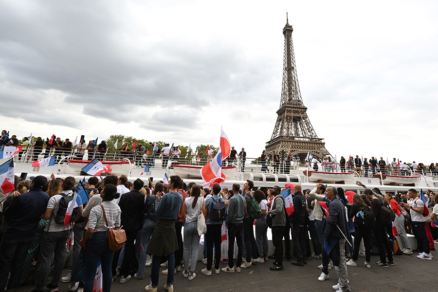 Taustalla Eiffel-torni ja kuvan edustalla iso joukkue väkeä Ranskan lippujen kanssa.