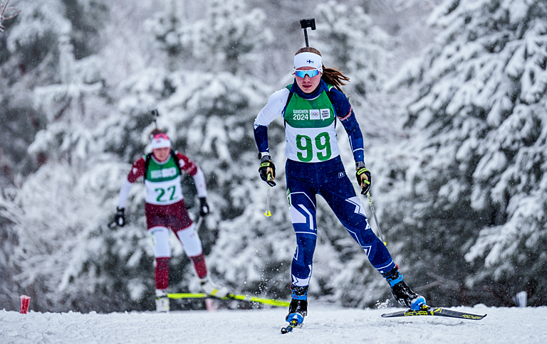 Ampumahiihtäjä Ilona Rantakömi hiihtämässä lumisateessa. Takana muiden maiden urheilijoita.